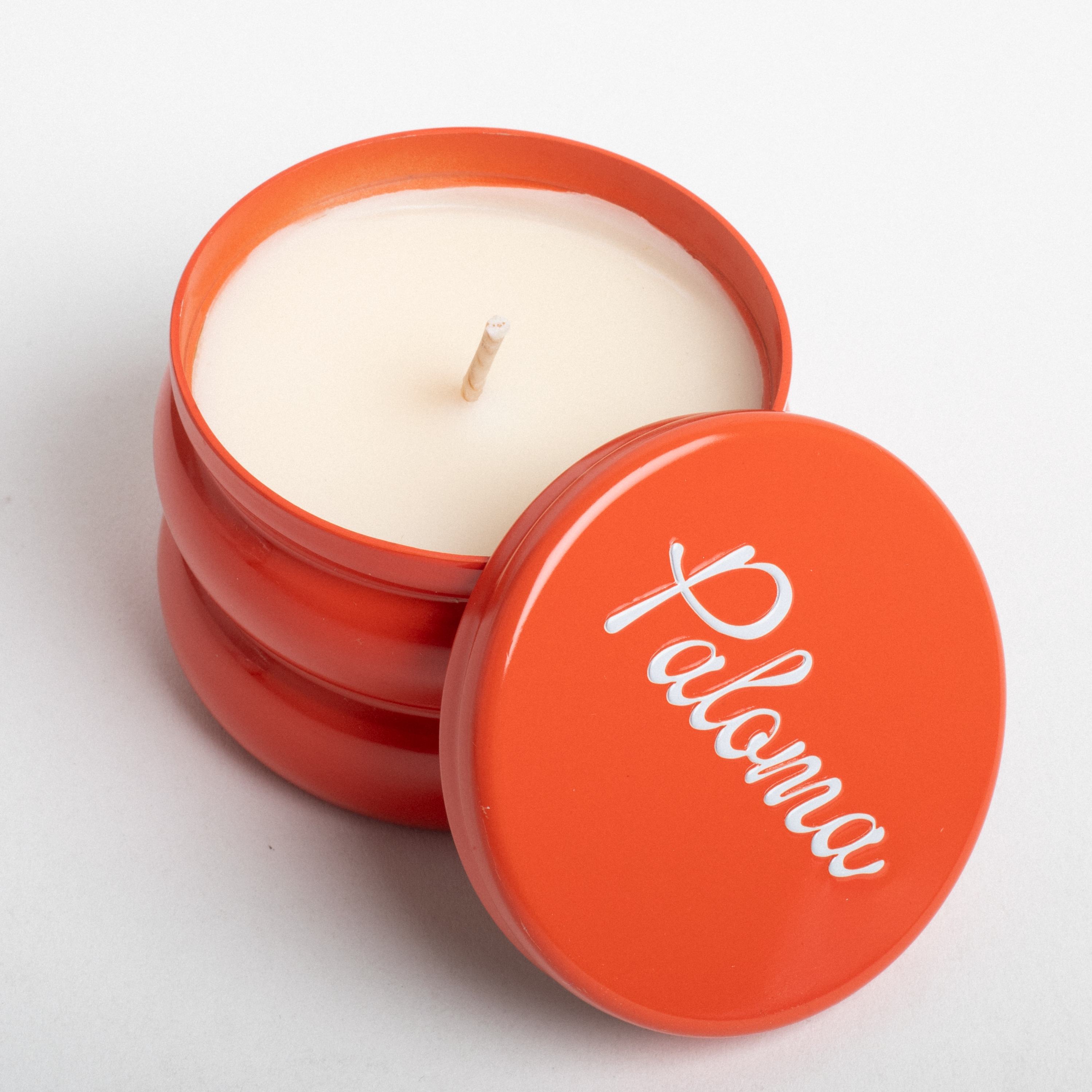 Candle in an orange container with 'Paloma' branding on a light gray background