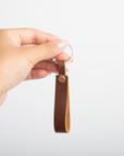Hand holding a brown leather keychain against a white background