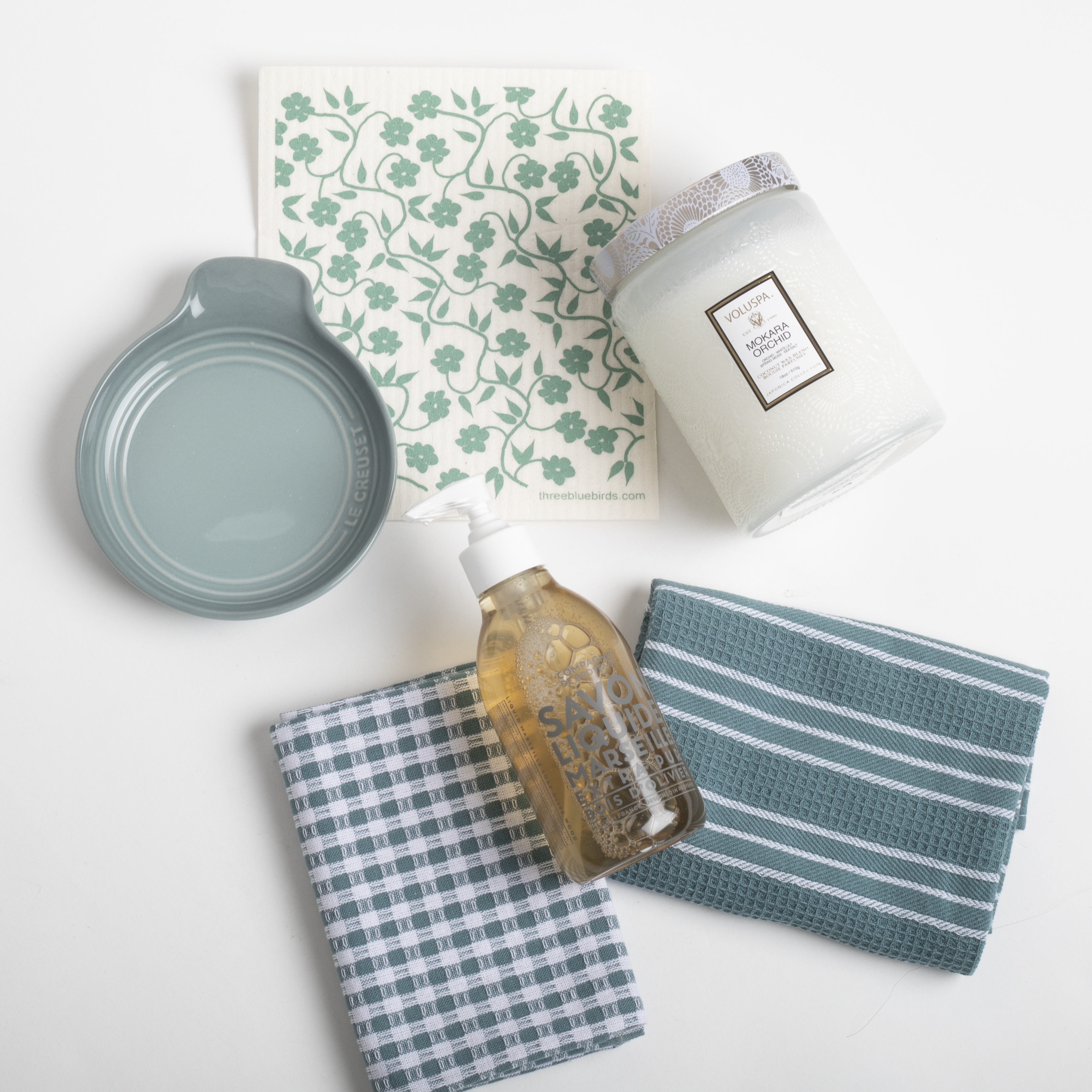 Collection of kitchen items including a candle, soap bottle, and cloths on a white background
