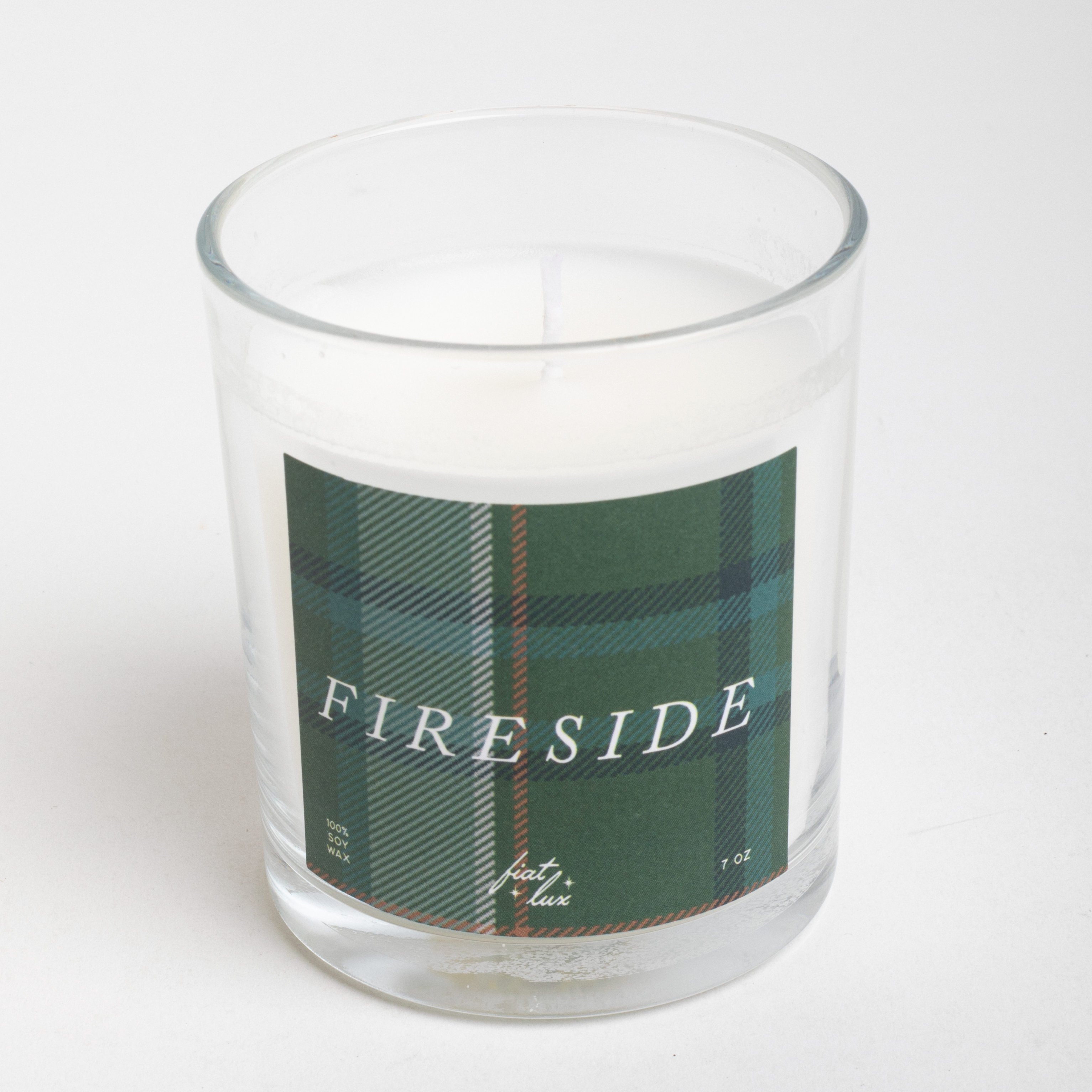 Clear glass candle with plaid label and 'FIRESIDE' text on a white background