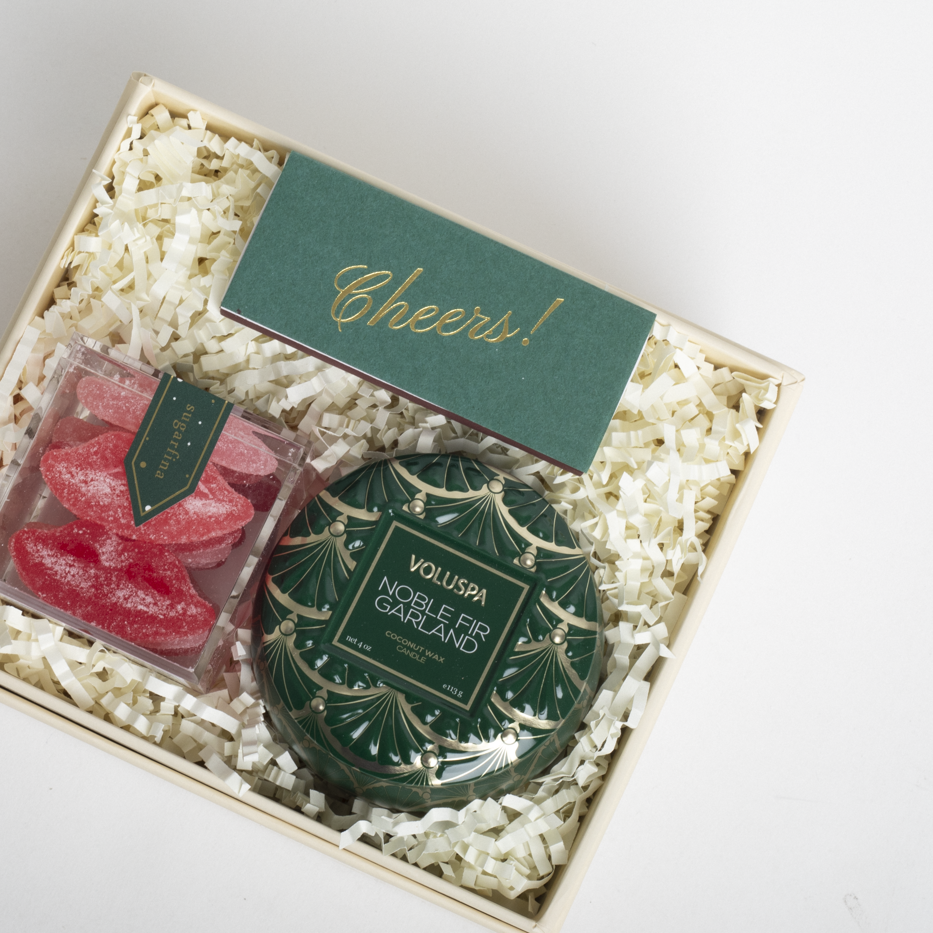 Gift set with Voluspa candle and red candy in a box labeled 'Cheers!'