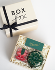 Gift box with 'Box Fox' branding, black ribbon, and a small green card inside.
