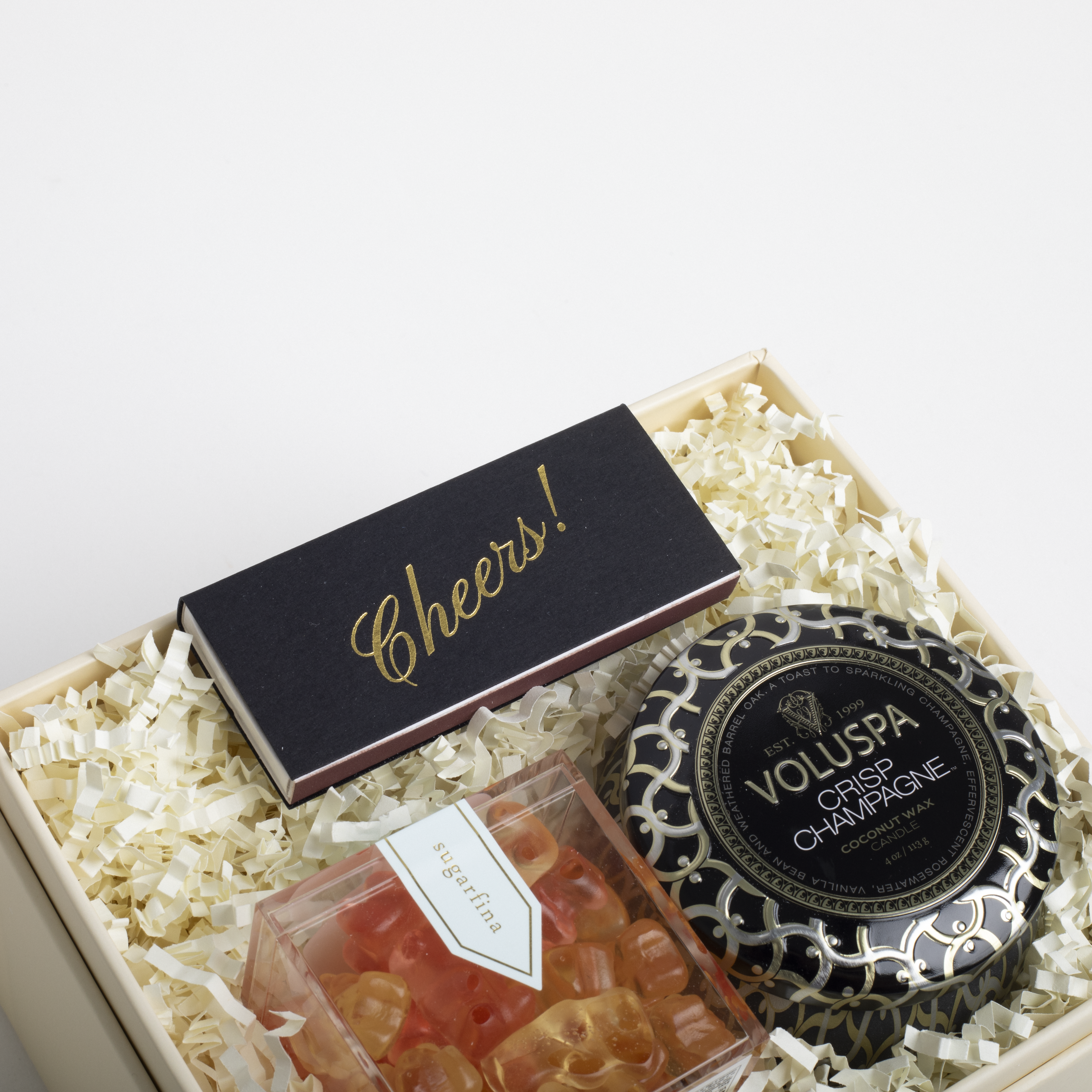 Gift set with Voluspa candle, &#39;Cheers!&#39; card, and small container of gummy bears in a box.
