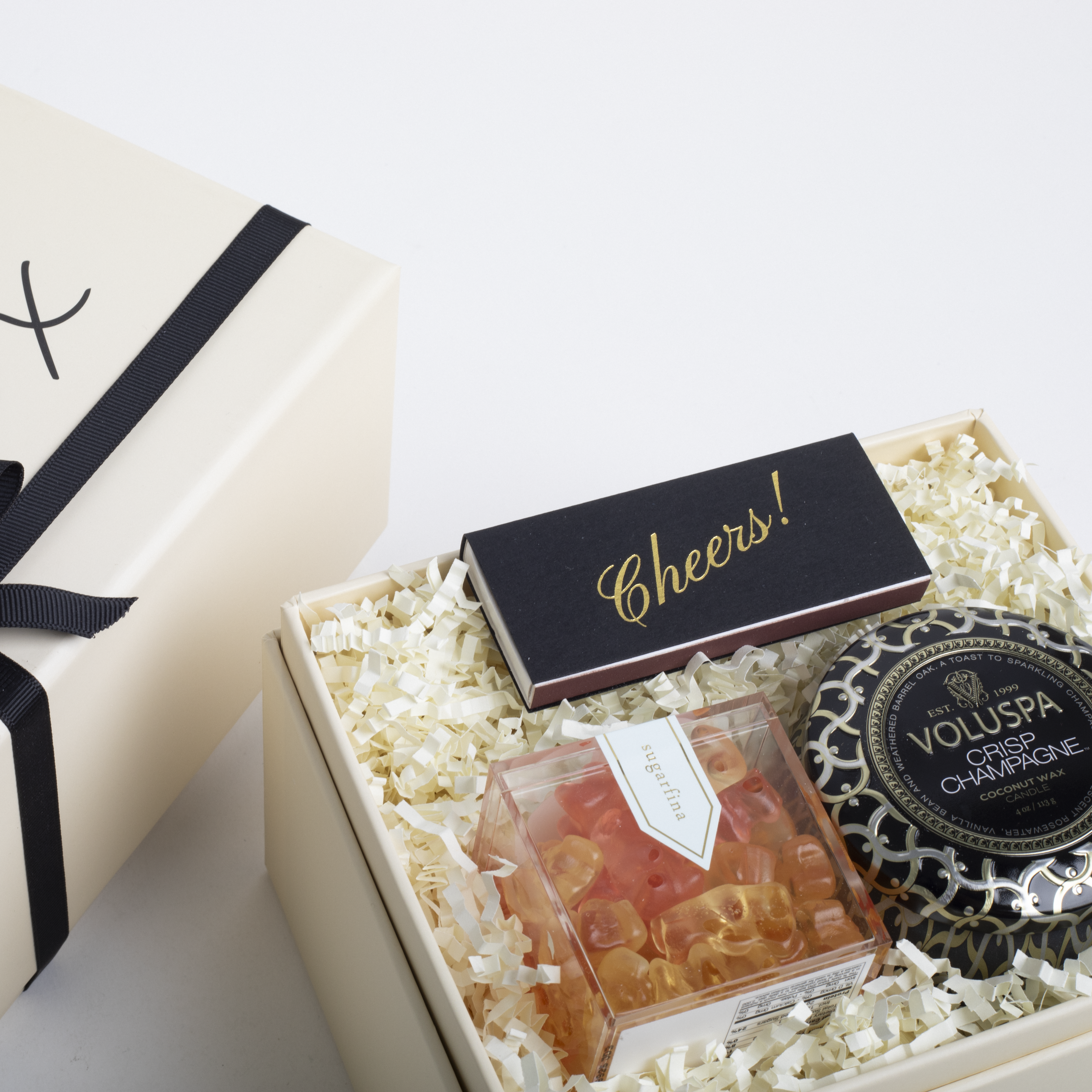 Gift box with gummy bears, chocolate bar, and Voluspa candle on a light background