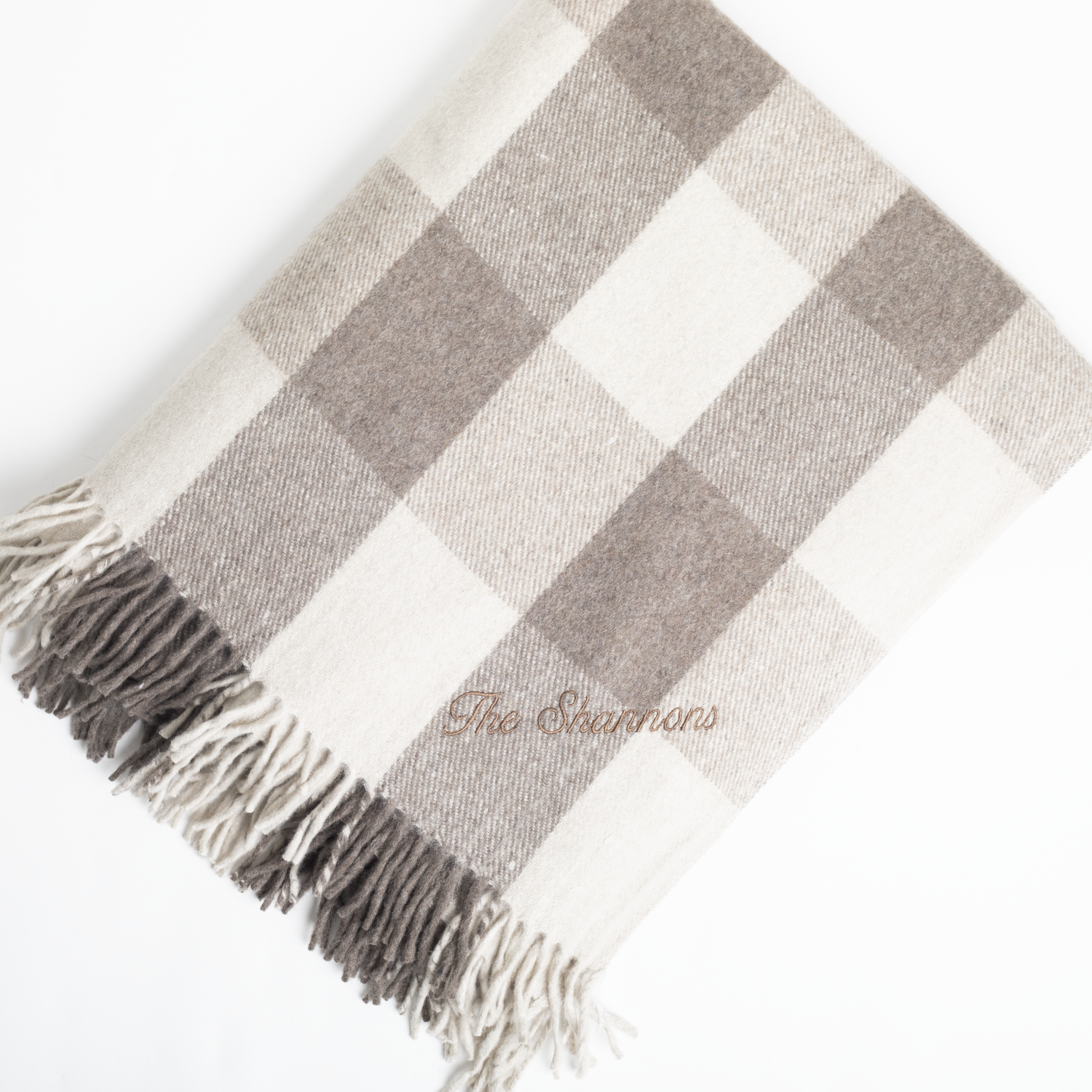 Plaid blanket with fringes and 'The Sweaters' branding on a white background