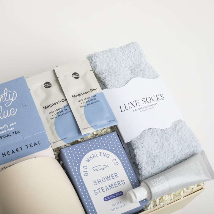 Assorted self-care items including tea packages, socks, and shower steamers in a box on a white background.