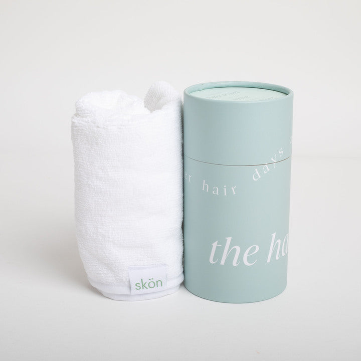 White hair towel and light blue cylindrical container with 'skön' branding on a white background