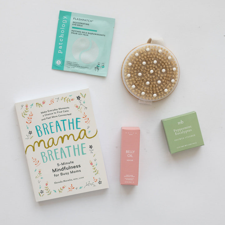 Collection of self-care products including a book, patch, oil, and pebbles on a white surface