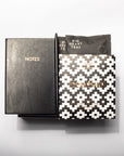 A Sea Salt tea gift set featuring a black textured notebook with gold lettering, a black tea sachet, and a black-and-white geometric patterned box, arranged on a light gray background.
