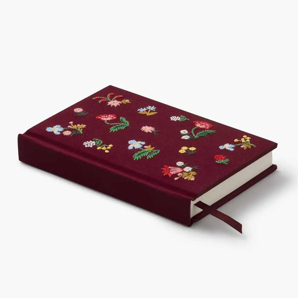 A hardcover notebook in deep burgundy velvet with colorful embroidered floral patterns on the cover, shown on a clean white background.