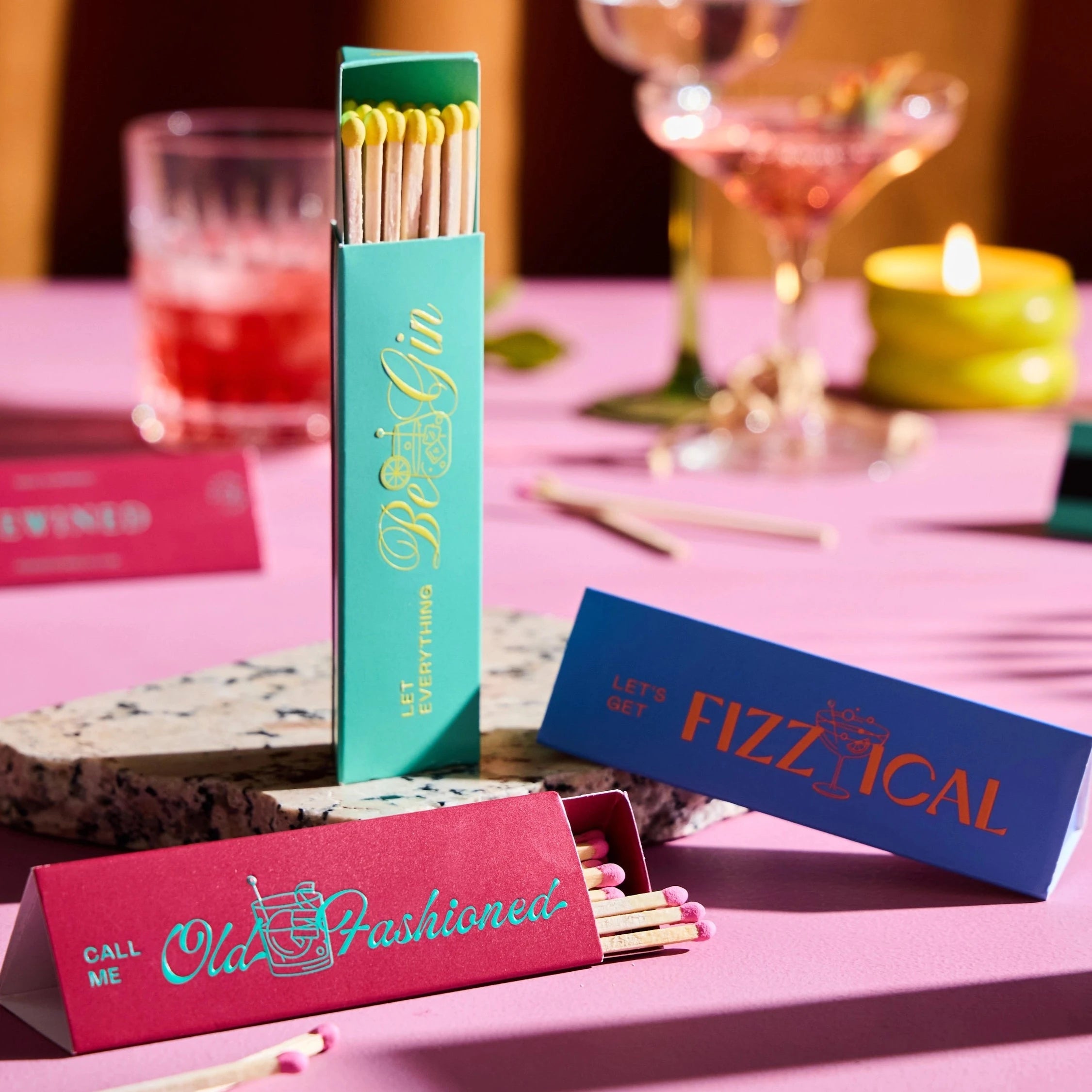 3 Matchboxes: Turquoise with "Be Gin" written on it in Yellow, Blue with "Fizzical" written on it in Red, and Magenta with "Old Fashioned" written on it in Turquoise