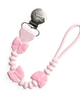 Pink pacifier clip with bow designs on a white background