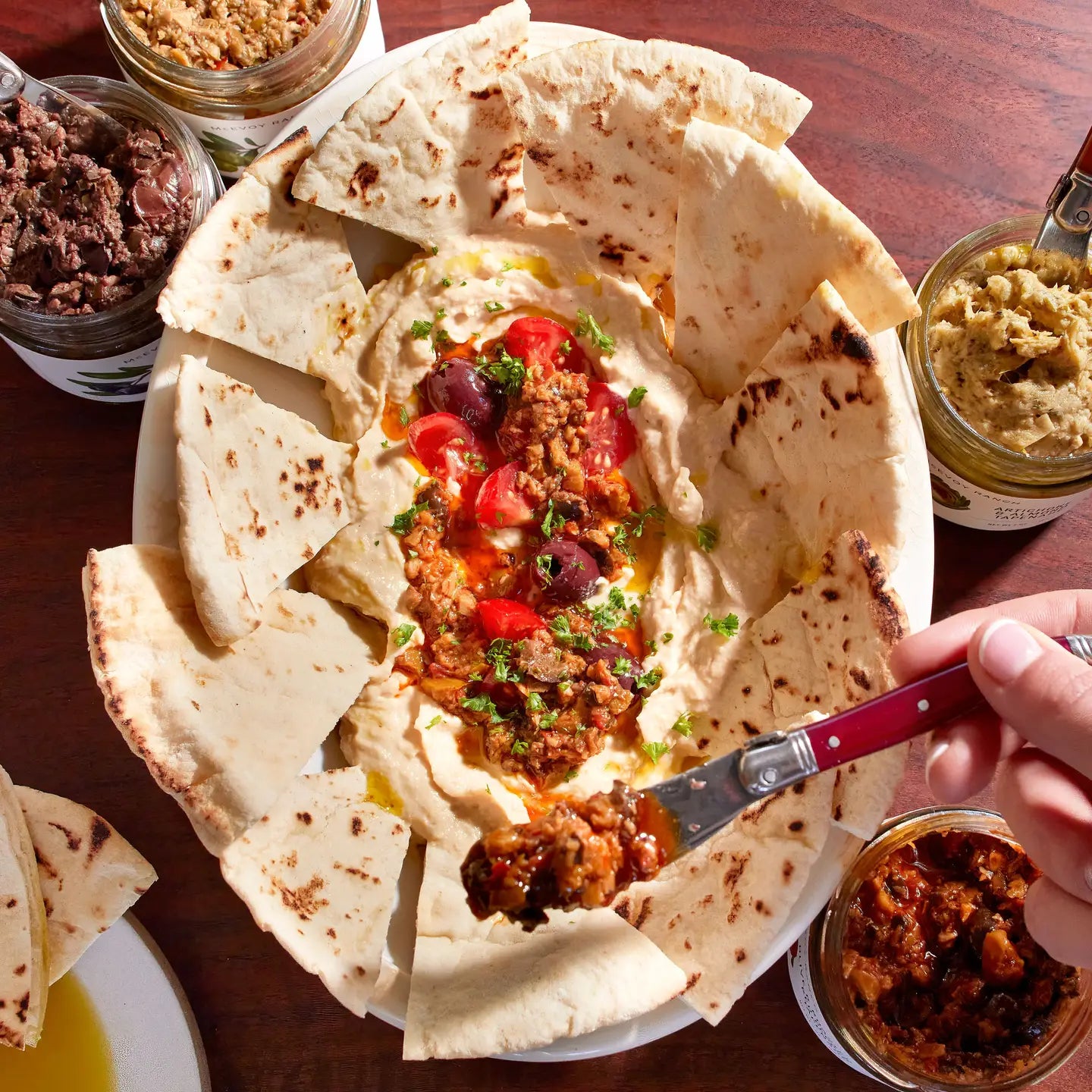 Platter of hummus with pita bread and various spreads on a wooden table