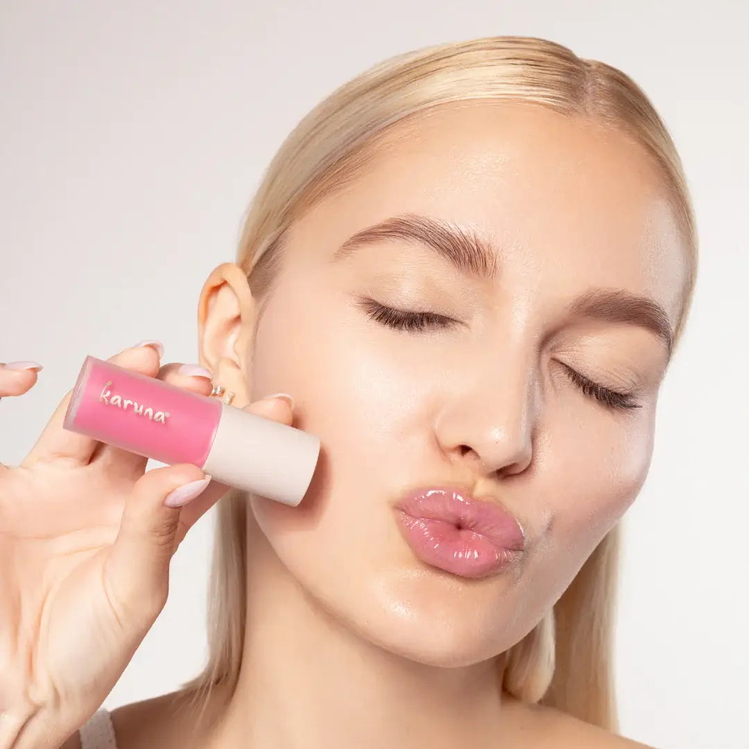 Woman holding a pink lip balm with 'karuna' branding against a neutral background