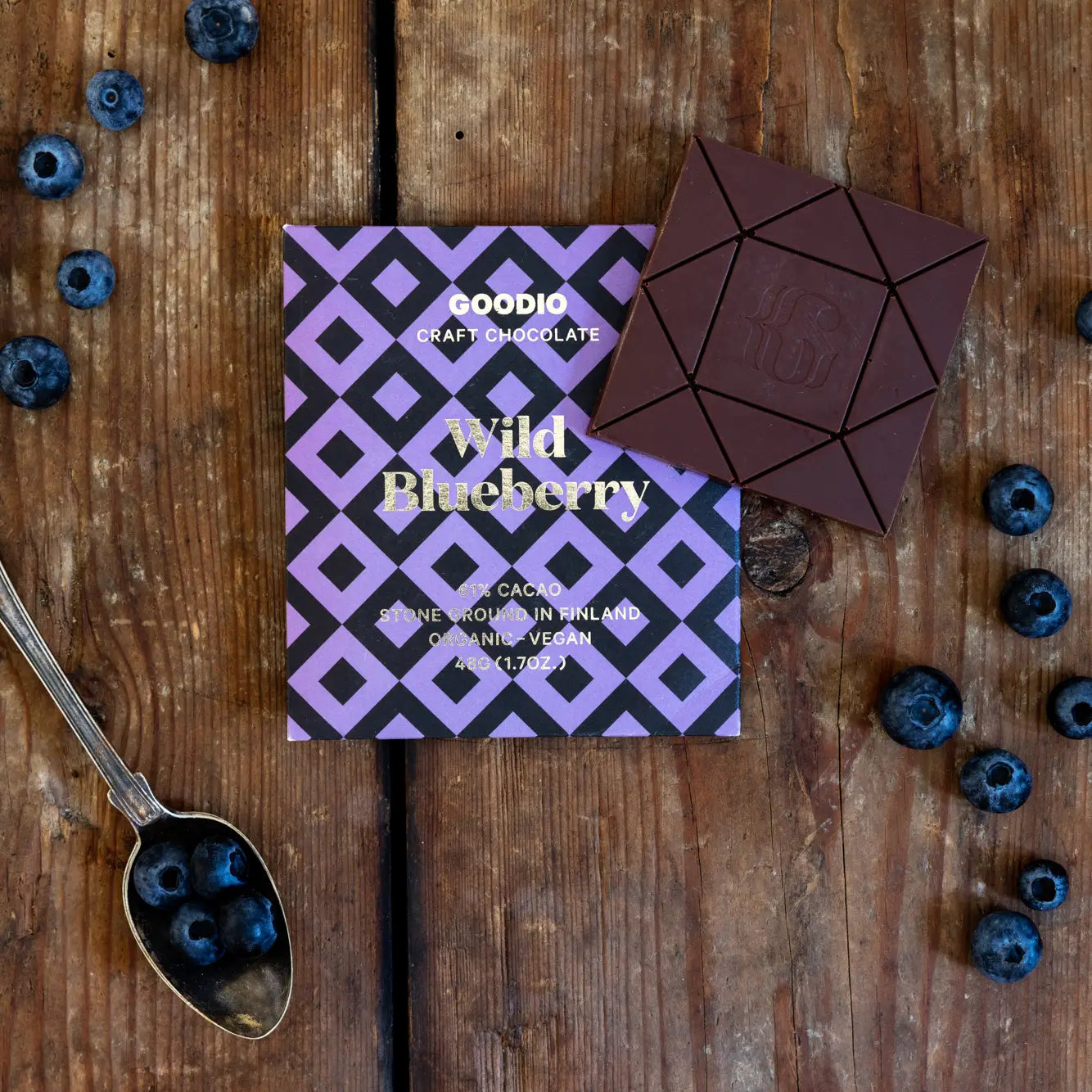 Goodio Wild Blueberry chocolate bar on a wooden surface with blueberries and a spoon.