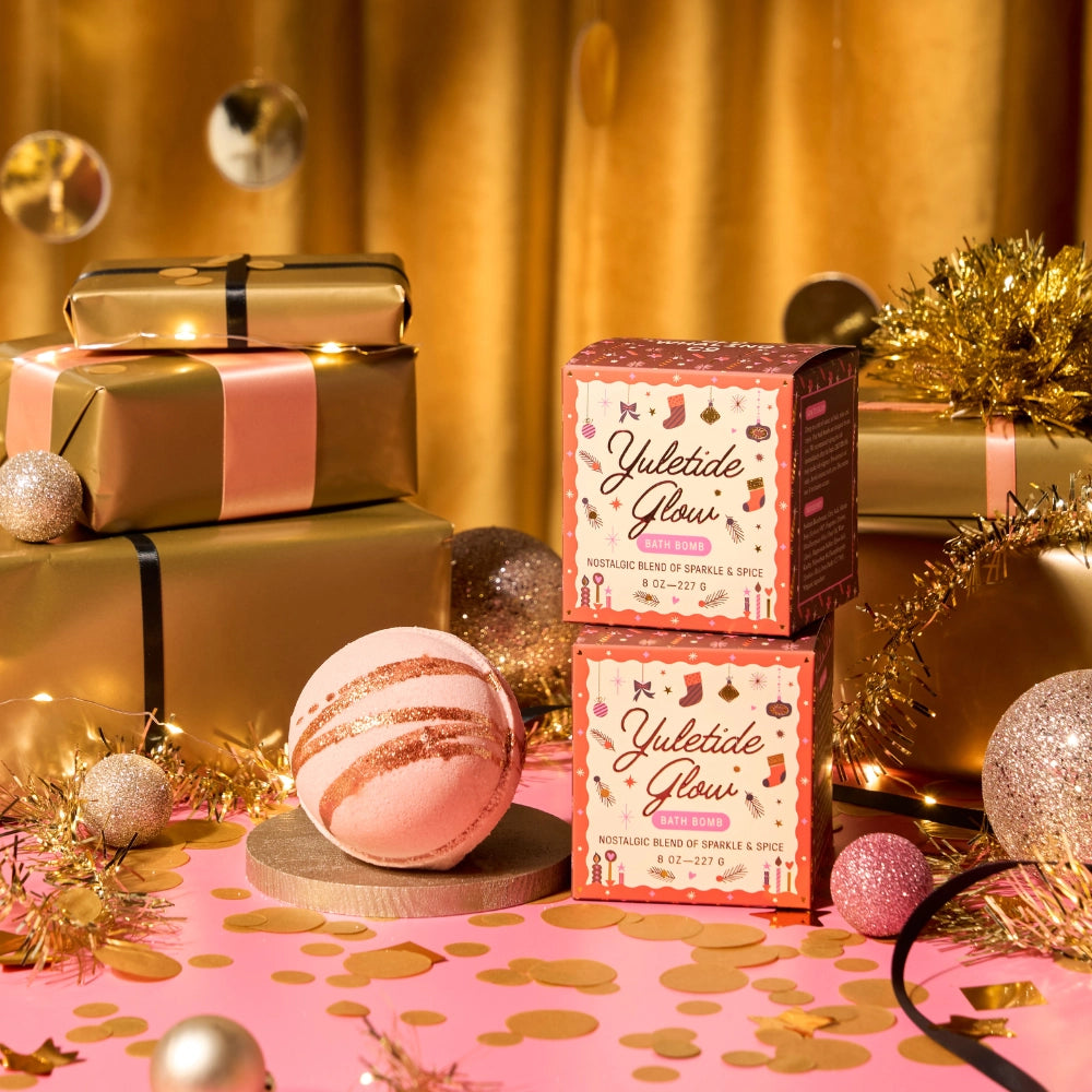 Bath bombs and packaging labeled 'Yuletide Glow' on a festive background with gold and pink decorations.