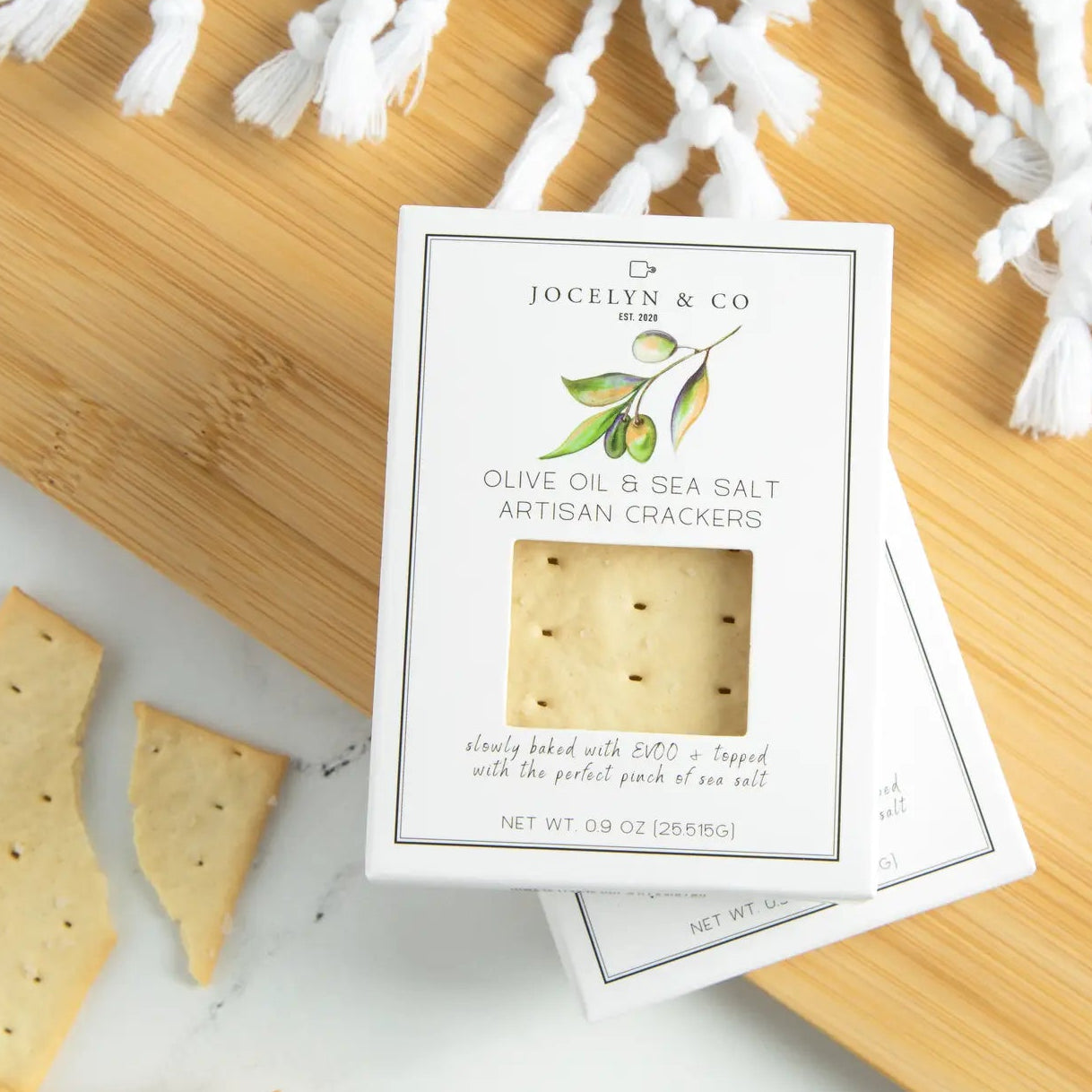 Olive oil and sea salt artisan crackers with packaging on a wooden surface.