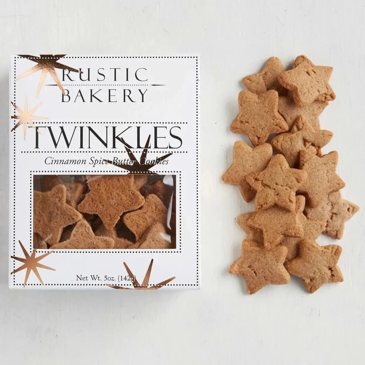 star shaped cookies in a pile next to a white box. Box is white with copper foil stars scattered around it. Box has black text and cut out window showing the cookies inside