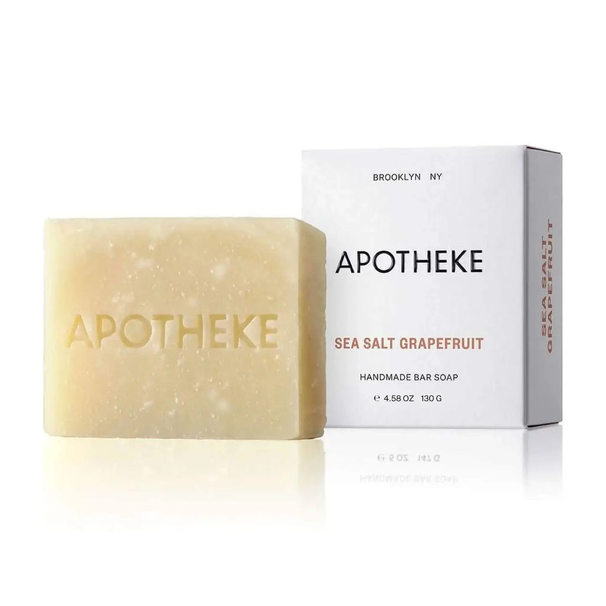 A pale yellow bar of Apotheke Sea Salt Grapefruit handmade bar soap stands in front of its white packaging box on a clean white background.