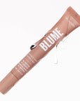 The image shows a tube of "Blume Superbalm" in a soft, beige-pink color. The product label mentions the scent or flavor as "Vanilla Cream" and highlights that it contains a "Tri-Peptide" formula, suggesting nourishing or restorative properties. The tube has a glossy finish, with some transparent liquid droplets running down the side, giving it a fresh, hydrating appearance. The volume is indicated as 12 mL (0.41 fl oz). The clean, minimal background emphasizes the elegance and sleek design of the balm.
