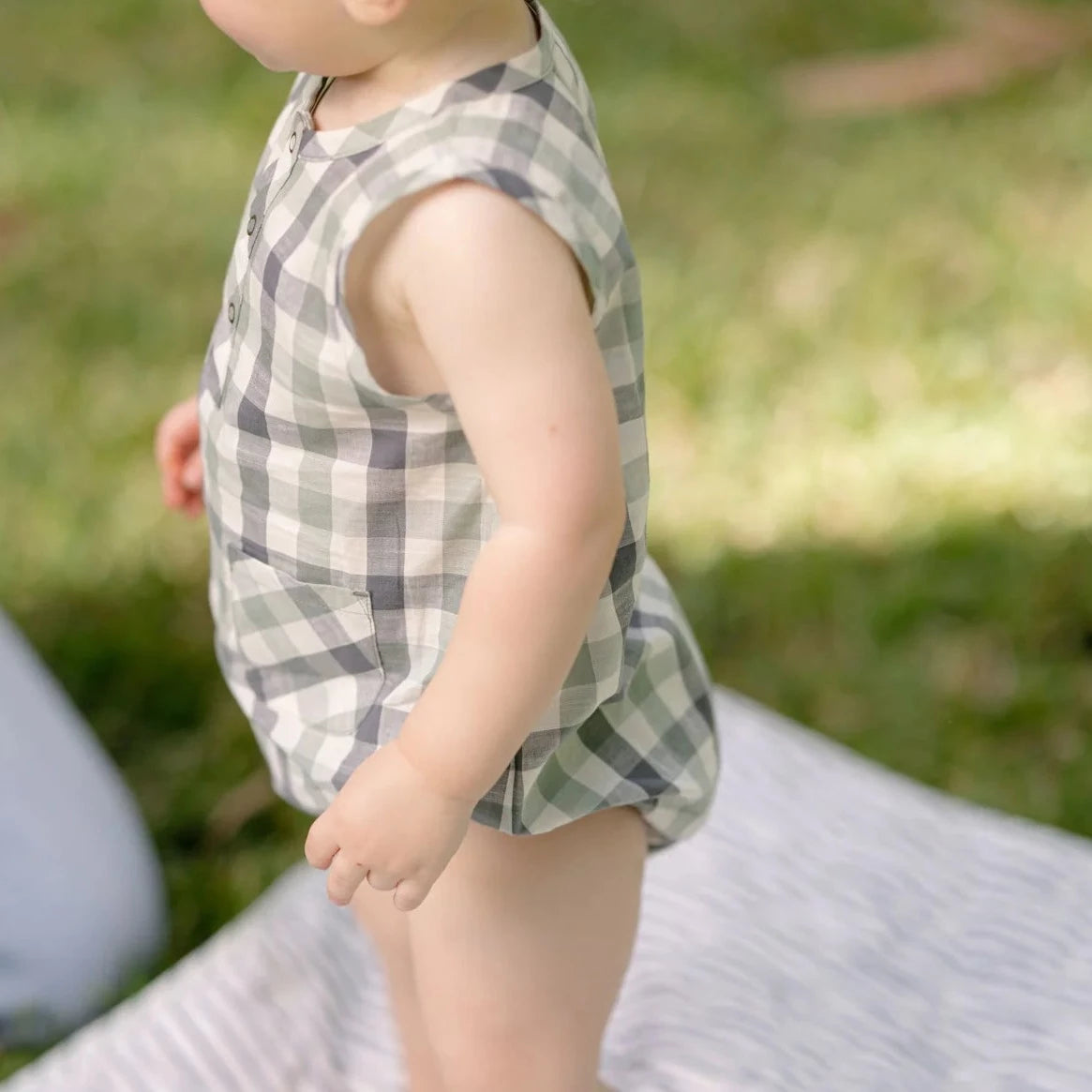 Baby wearing checkered romper on standing on grass