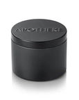 A small matte black cylindrical container with a matching lid, featuring the brand name 'APOTHEKE' embossed on top, set against a solid white background.