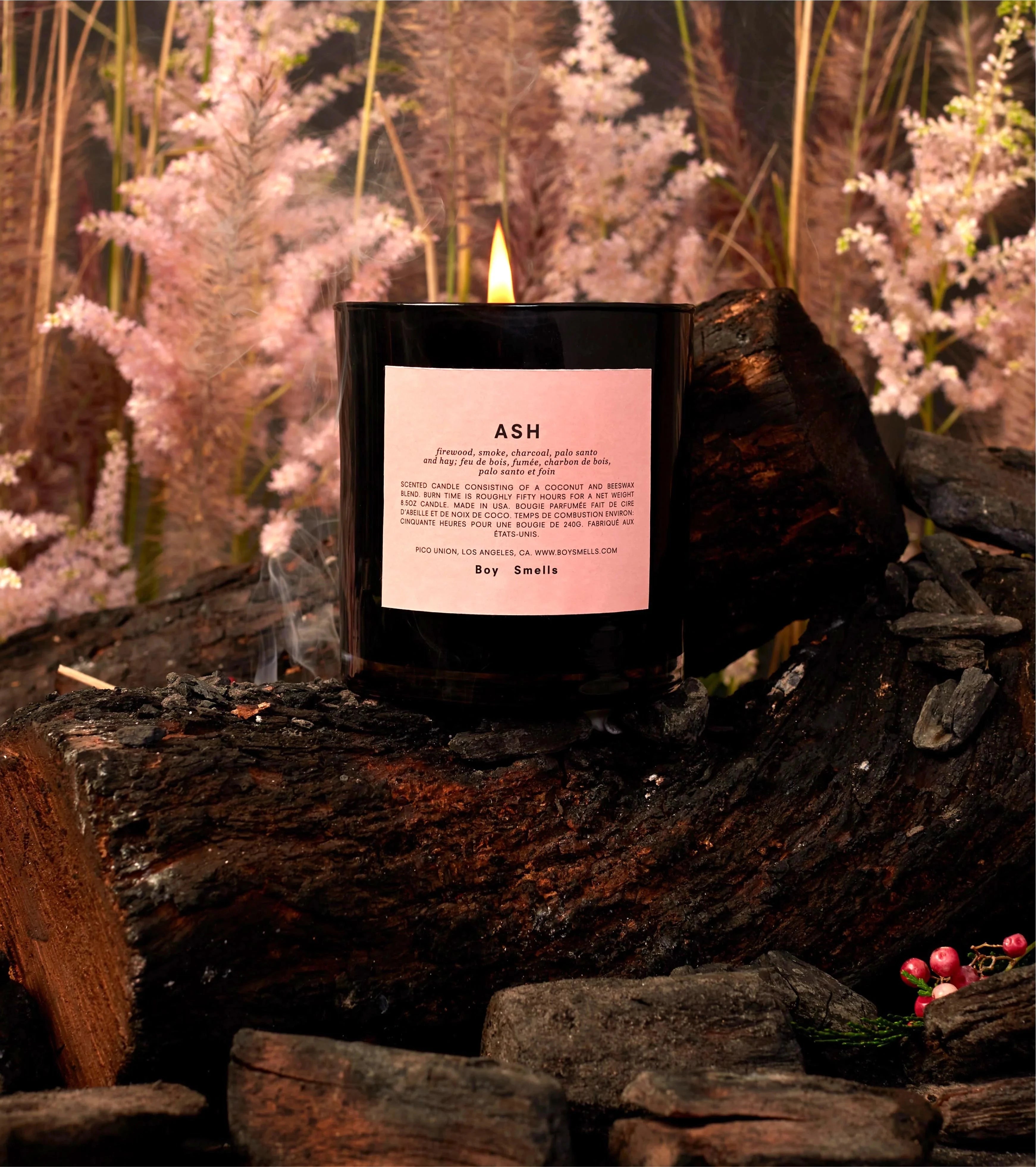 pink woodsy background with black candle on fire wood. candle has pink label on the center