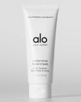 A white tube of "Alo Glow System Restorative Hand Cream" standing upright against a plain light background. The label highlights key ingredients such as amla, squalane, shea butter, and arnica, promoting it as part of a clean beauty regimen.