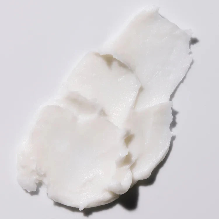 A close-up of a smear of thick, creamy white hand cream spread across a smooth surface. The texture appears rich and moisturizing, emphasizing the cream's nourishing properties.

