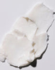 A close-up of a smear of thick, creamy white hand cream spread across a smooth surface. The texture appears rich and moisturizing, emphasizing the cream's nourishing properties.

