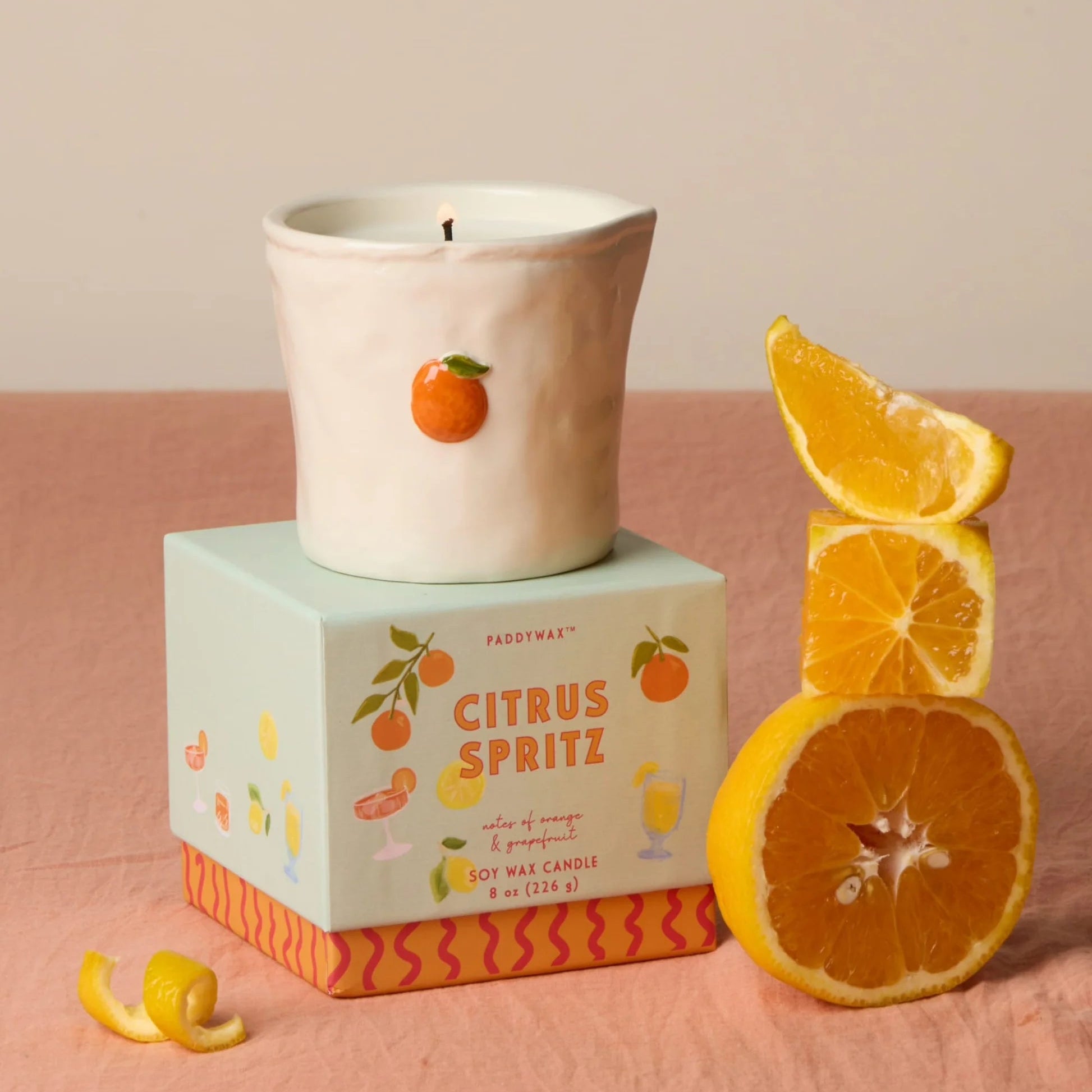 Candle with a citrus spritz theme on a pink surface