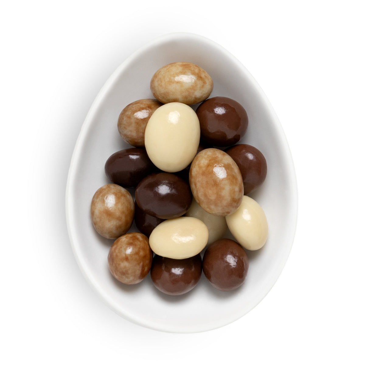 A top-down view of assorted chocolate-covered jelly beans in dark brown, milk brown, and white, presented in a white ceramic egg-shaped dish on a white background.