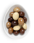 A top-down view of assorted chocolate-covered jelly beans in dark brown, milk brown, and white, presented in a white ceramic egg-shaped dish on a white background.