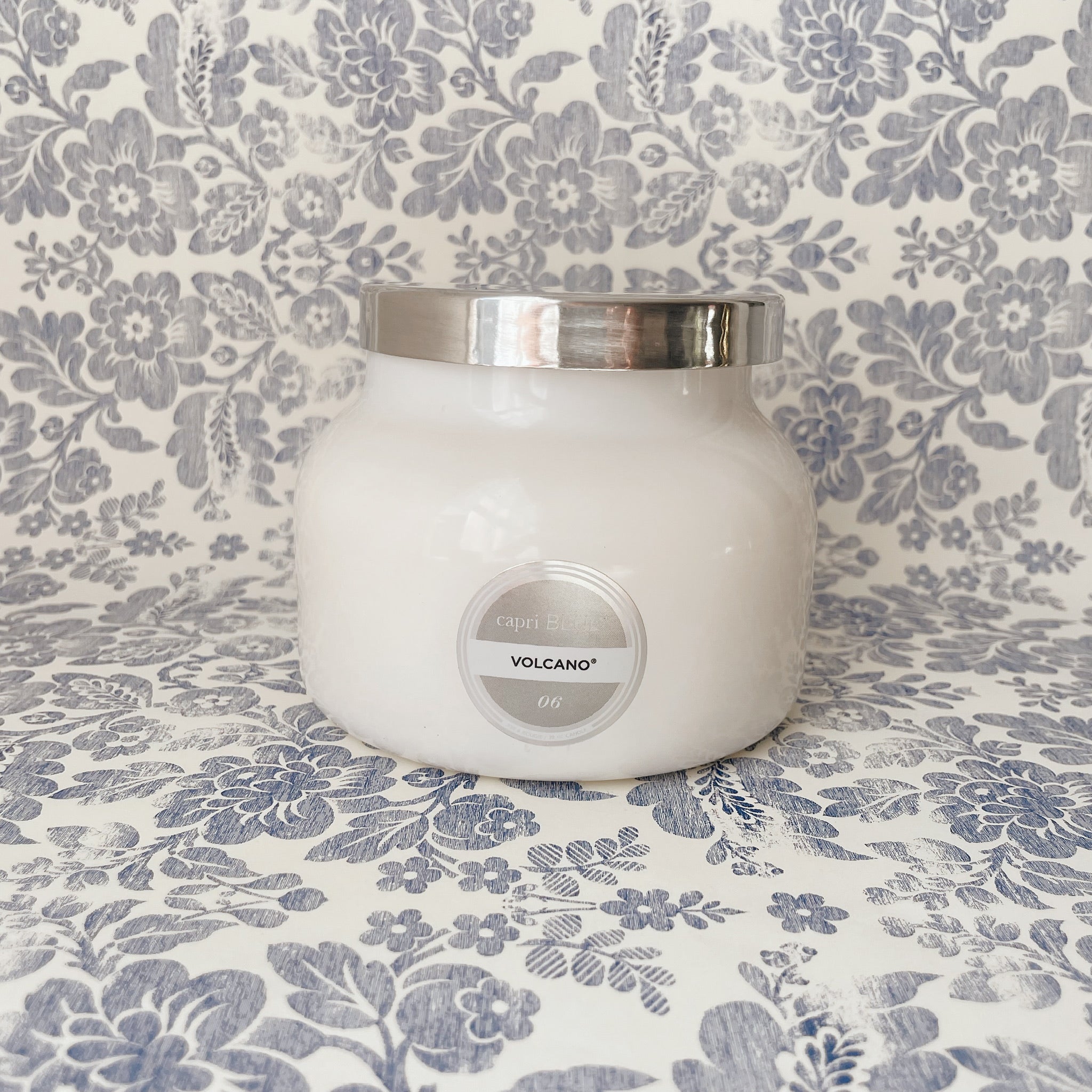 White glass jar candle with silver lid on a blue and white floral backdrop.