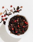 White bowl filled with black tea leaves and red berries on a light background