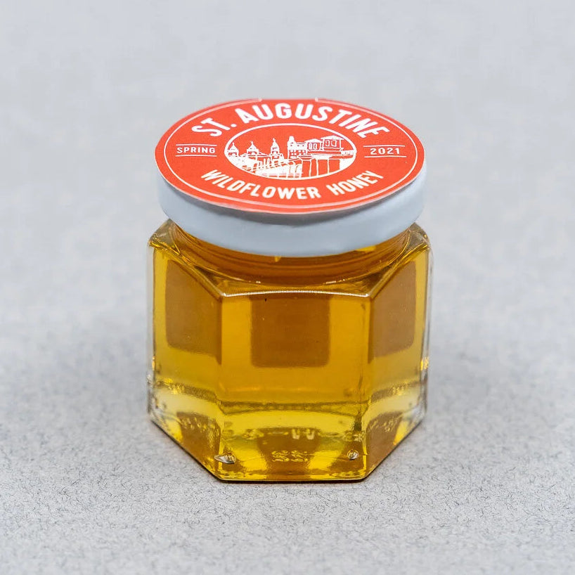 Hexagonal jar of honey with a red label on a light gray background