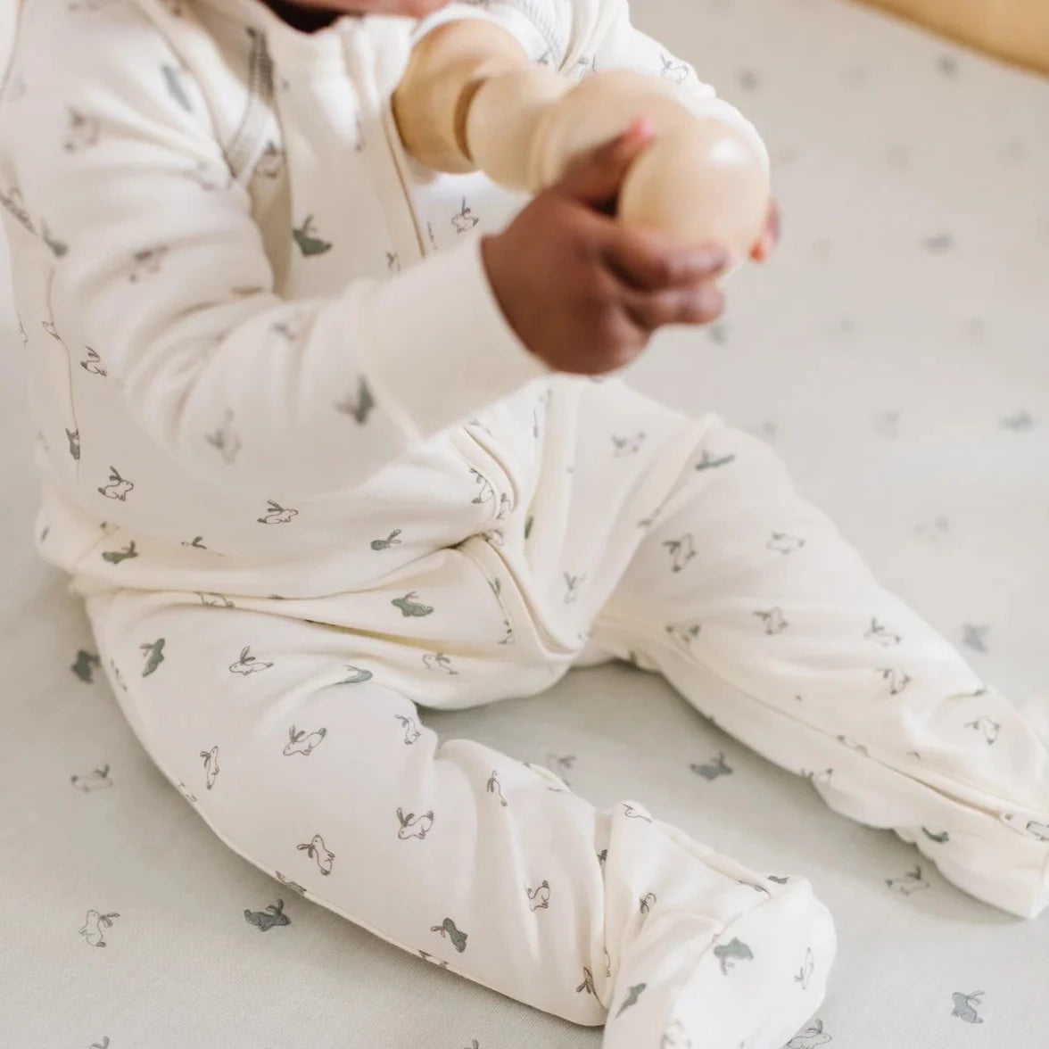 baby sitting in crib wearing hatchling bunny pajamas.