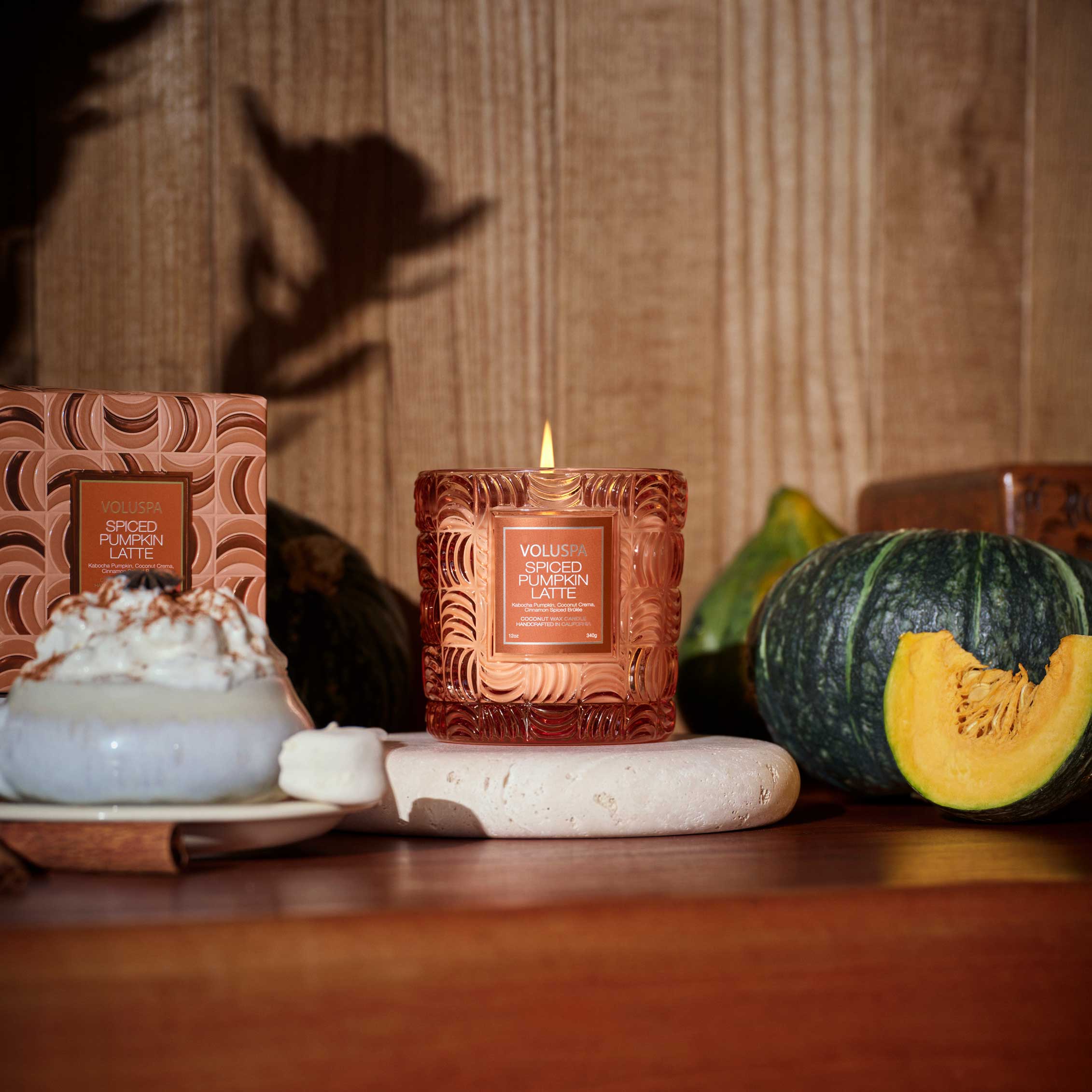 Candle with decorative packaging on a table with pumpkins and a dessert.