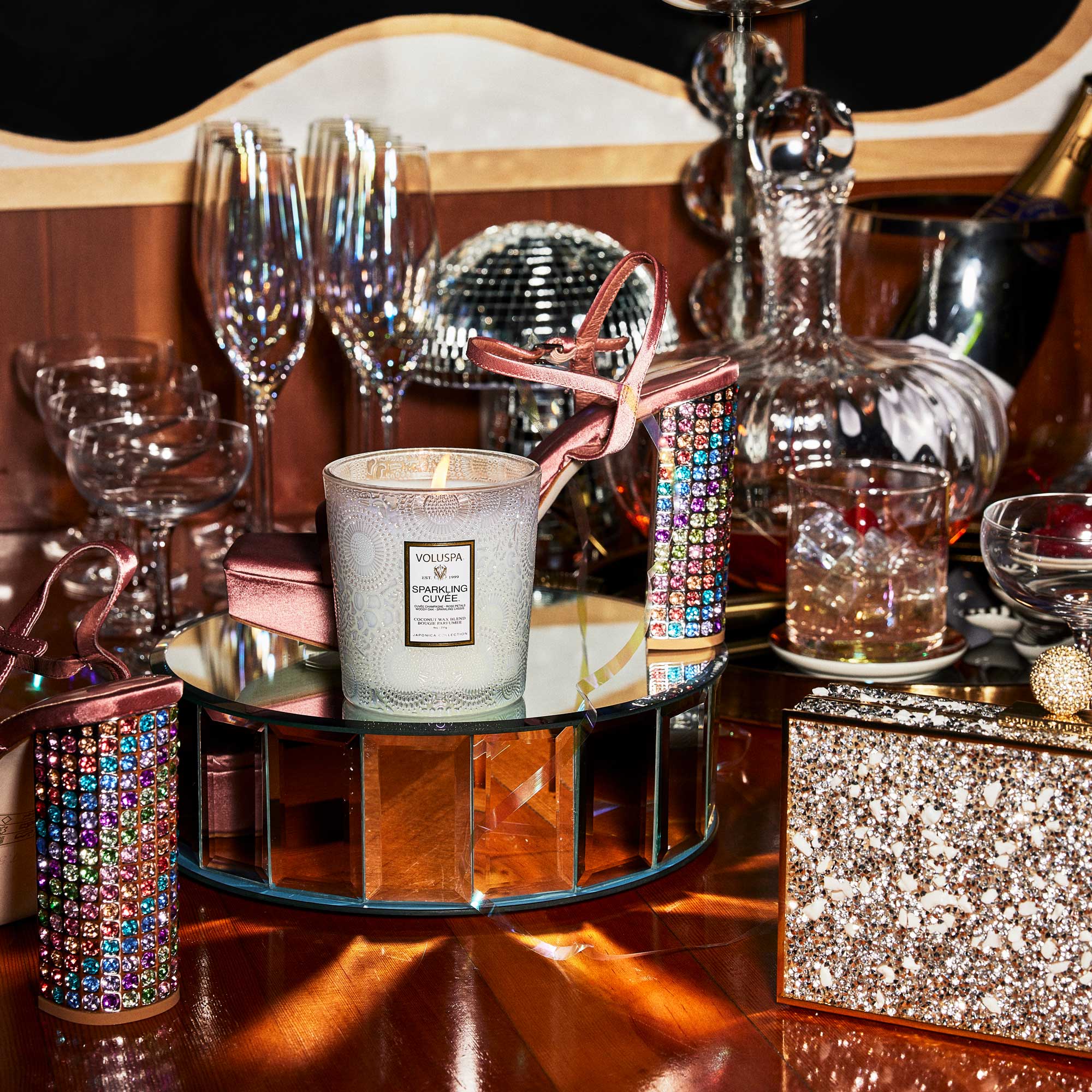 Decorative table setting with a candle, glasses, and decorative items on a reflective surface.
