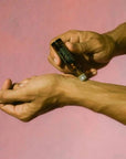 hand rolling oil on wrist on a pink background