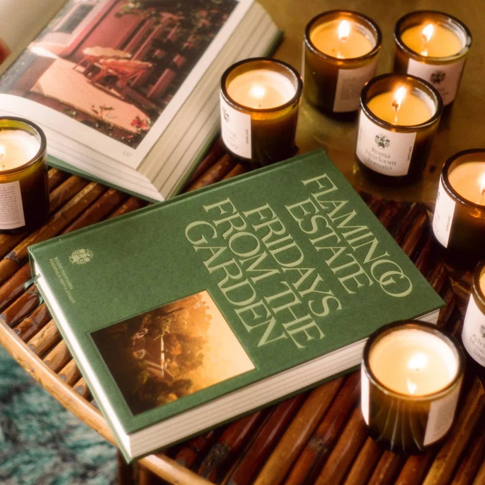 Green book titled 'Flamingo State Fridays from the Garden' on a wooden table with lit candles.