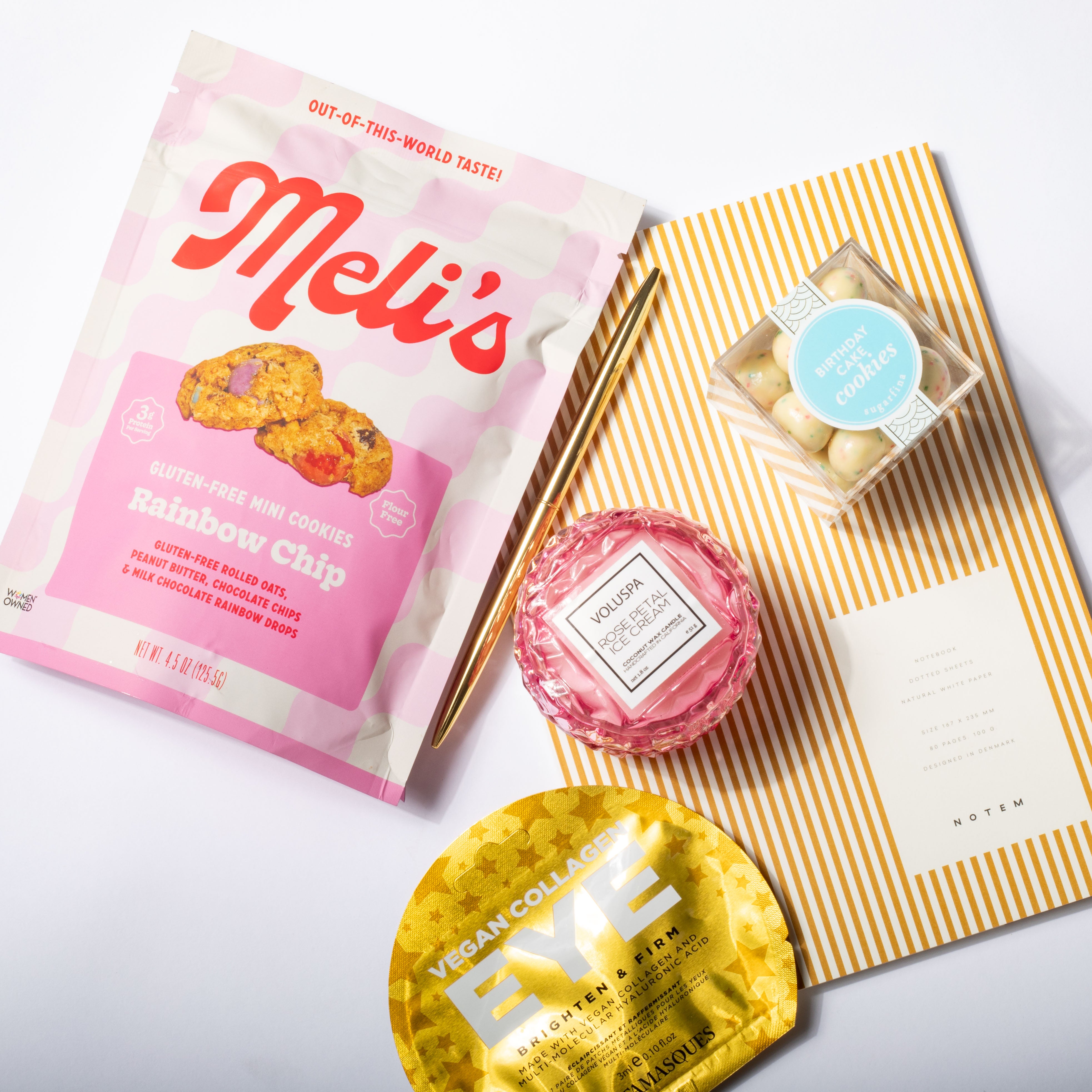 Meli's cookie package with a pink and gold product, and a striped napkin with a small dish on a white background.
