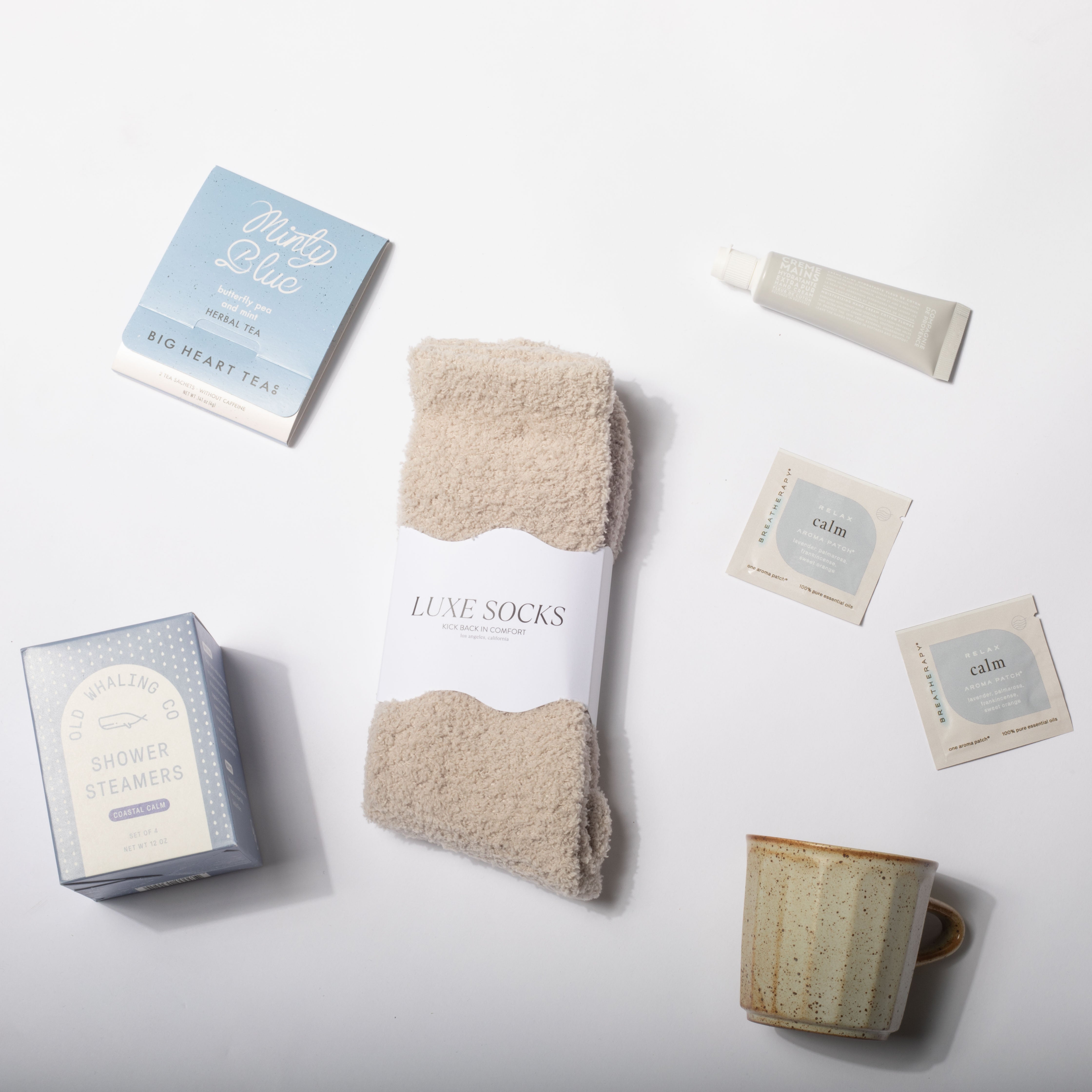 Set of beige luxe socks with tea boxes, a mug, and a tube on a white background