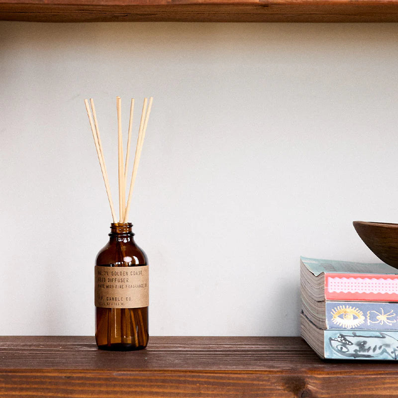 Brown diffuser bottle with wooden sticks on a wooden shelf against a white wall.