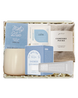 A curated self-care gift box set from Big Hearted Things, featuring a minty blue herbal tea packet, a calming bath soak packet, a shower steam packet, a comfort pack, a tube of natural nail care, and a beige ceramic candle, all arranged in a white gift box with shredded paper filler.