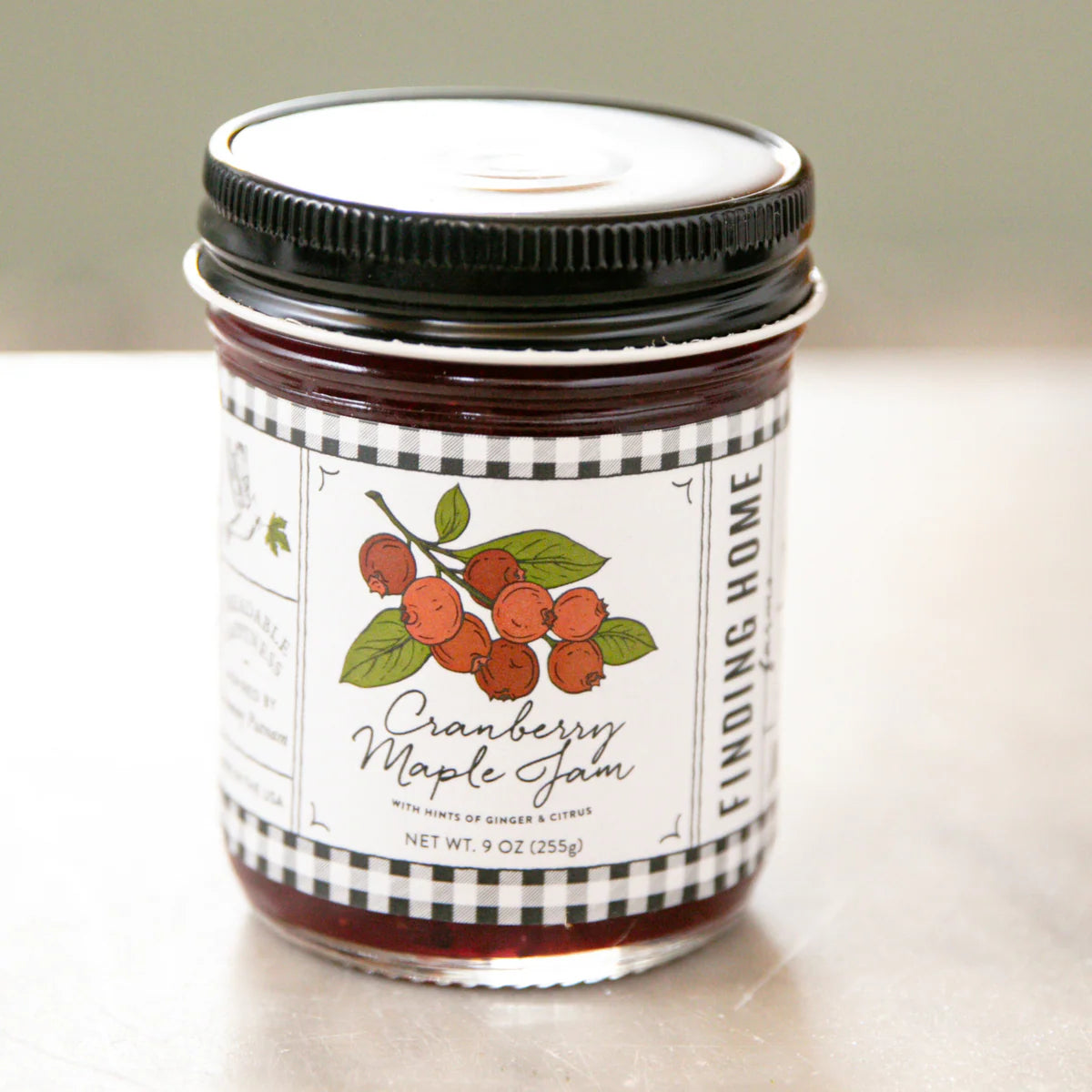 Jar of cranberry maple jam with a checkered label on a light background