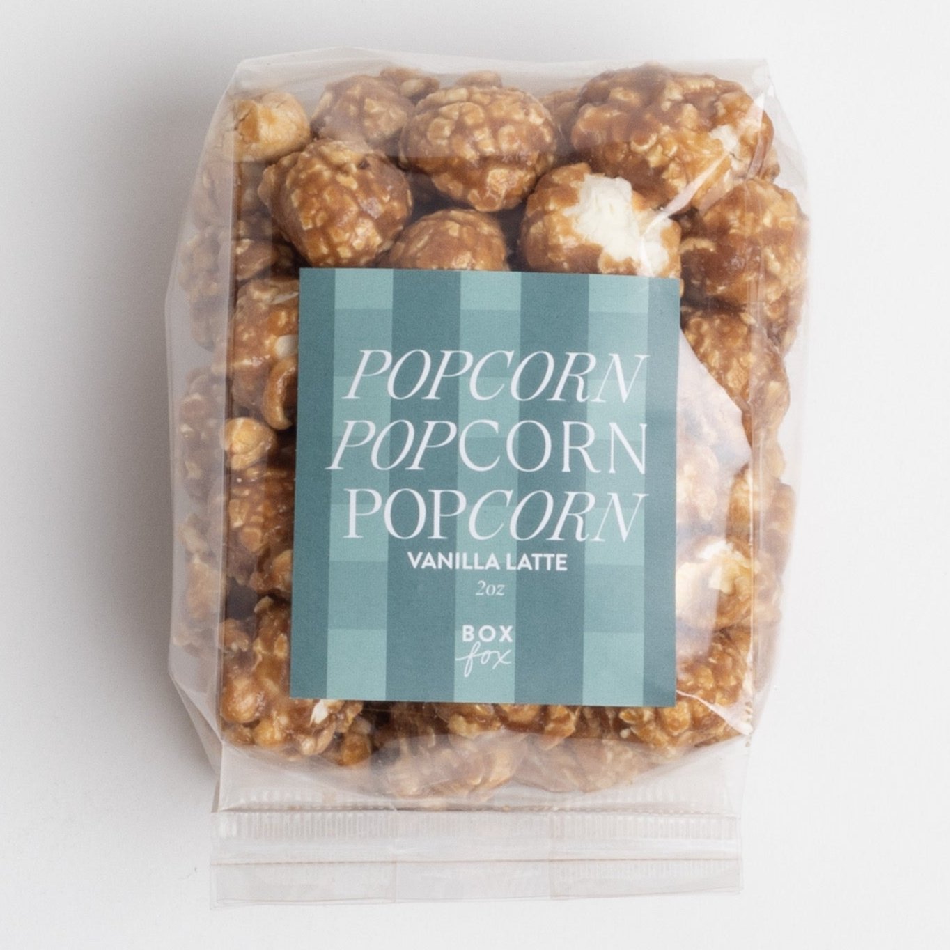 A clear bag of popcorn labeled &quot;Popcorn Popcorn Popcorn&quot; with a teal-striped design. The flavor is listed as &quot;Vanilla Latte,&quot; and the bag weighs 2 oz. The packaging is branded with the Boxfox logo at the bottom.