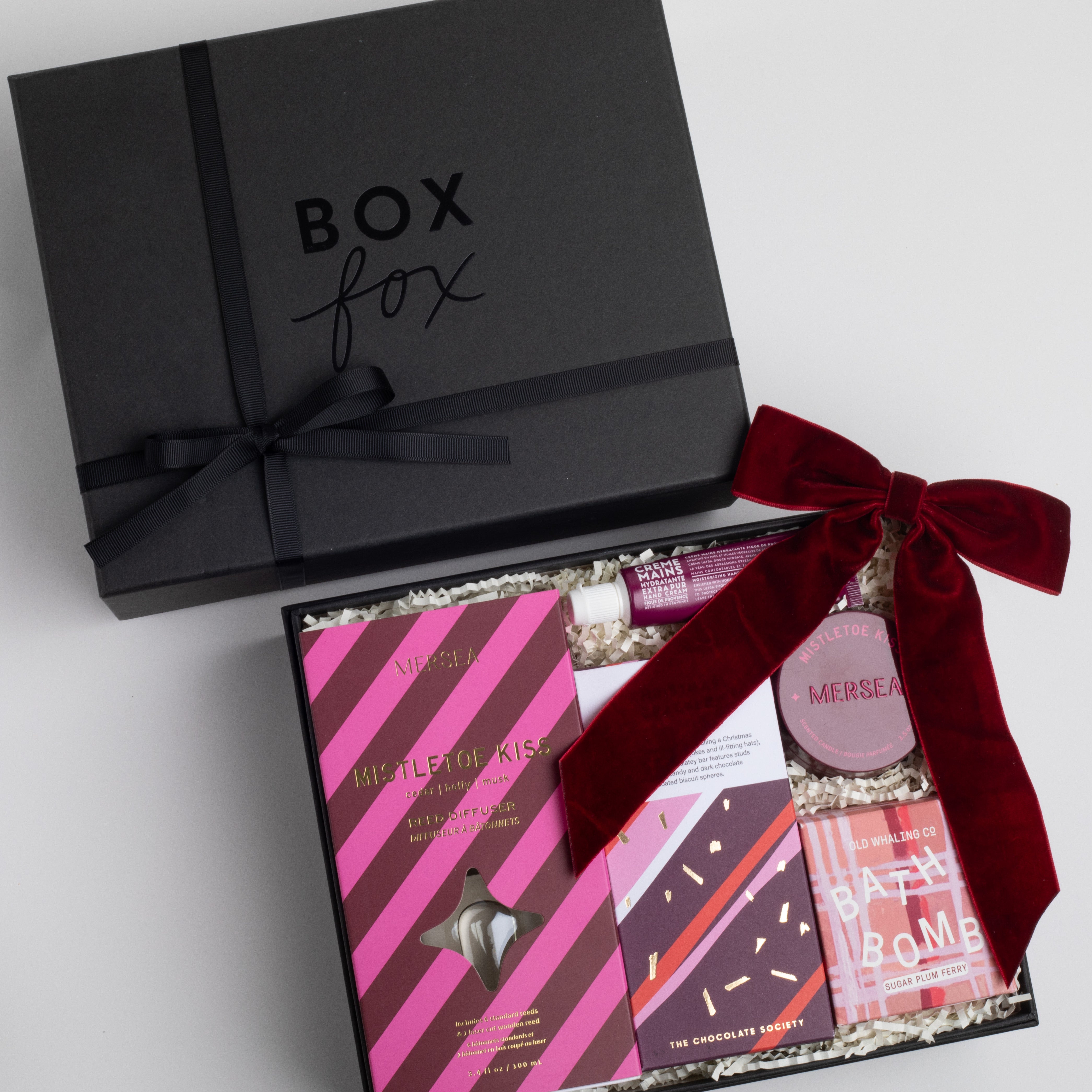 BLACK BOXFOX BOX DISPLAYED OPEN WITH: Mistletoe Kiss Reed Diffuser, Mistletoe Kiss Tin Candle, Christmas Cracker Bar, Sugarplum Ferry Bath Bomb, Maroon Velvet Bow Hair Clip, Fig of Provence Travel Hand Cream