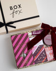 CREME BOXFOX BOX DISPLAYED OPEN WITH: Mistletoe Kiss Reed Diffuser, Mistletoe Kiss Tin Candle, Christmas Cracker Bar, Sugarplum Ferry Bath Bomb, Maroon Velvet Bow Hair Clip, Fig of Provence Travel Hand Cream