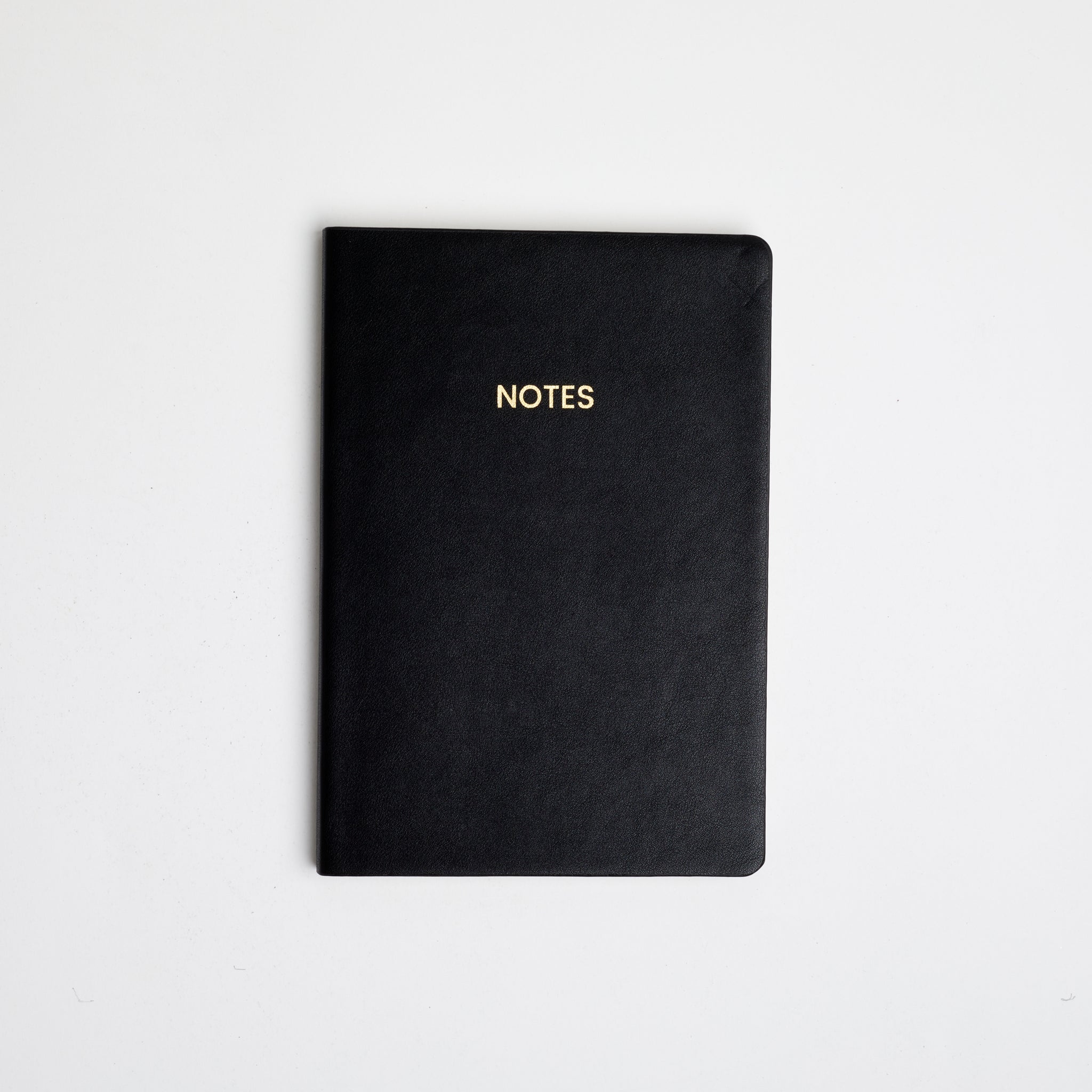 A black colored vegan leather notebook with gold foil text reading &quot;NOTES&quot; across the front photographed against a white background.